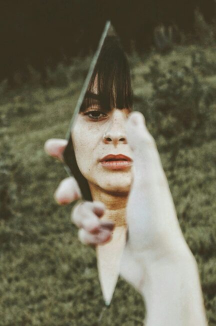 Artistic photo of a woman's reflection in a handheld broken mirror outdoors.