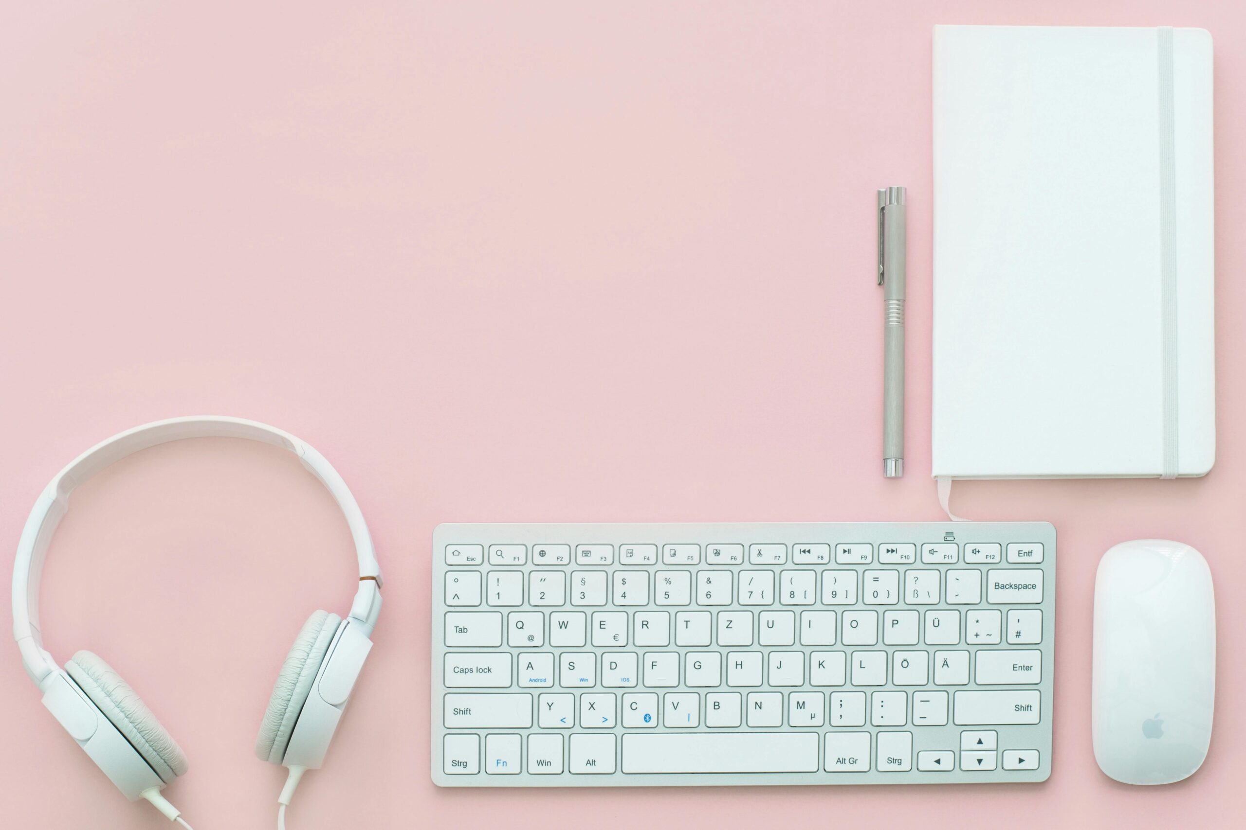 Elegant flat lay of white electronics and stationery on pastel pink background.