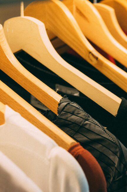 A close-up view of a row of clothes on wooden hangers, showcasing various fabrics and colors in a wardrobe setting.